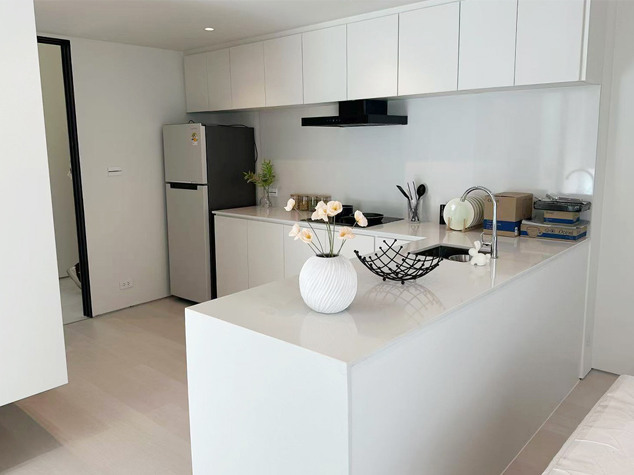 Project case image for an apartment project in Thailand. The image features an L-shaped kitchen with modern cabinetry, sleek countertops, and integrated appliances. The design combines functionality and style, using light, neutral tones to create a bright and efficient cooking space with a contemporary feel.