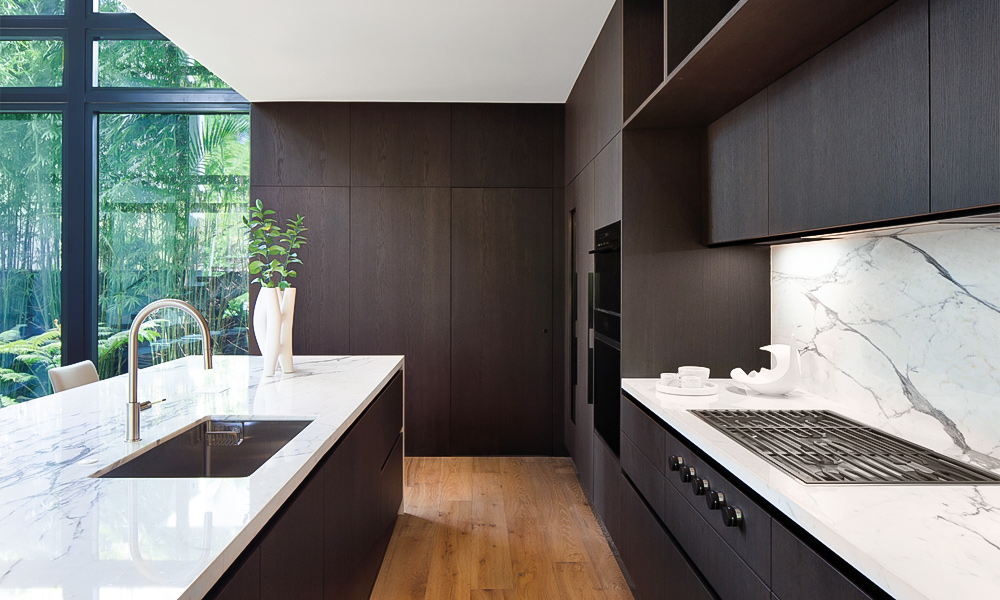 A sleek L-shaped kitchen with black wood veneer cabinets and a central countertop island. The deep black tones create a sophisticated and dramatic atmosphere, while the wood grain adds texture and warmth. The L-shaped layout maximizes space efficiency, and the central island enhances both functionality and modern style.