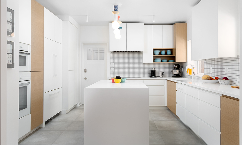 A close-up view of an L-shaped kitchen with white lacquered cabinets and a central island. The glossy white finish gives the space a bright and clean look, while the island adds functionality and a modern touch. The partial image highlights the sleek surfaces and minimalist design details.