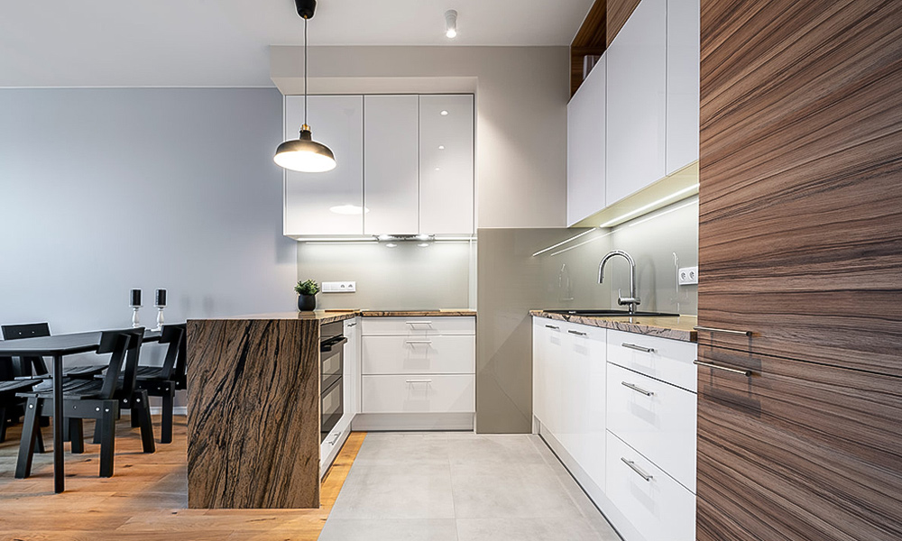 A close-up of a modern one-wall kitchen featuring white lacquered cabinetry and a white countertop central island. The sleek design highlights the clean, minimalist lines of the cabinetry and the smooth surface of the island, creating a bright and contemporary kitchen space.