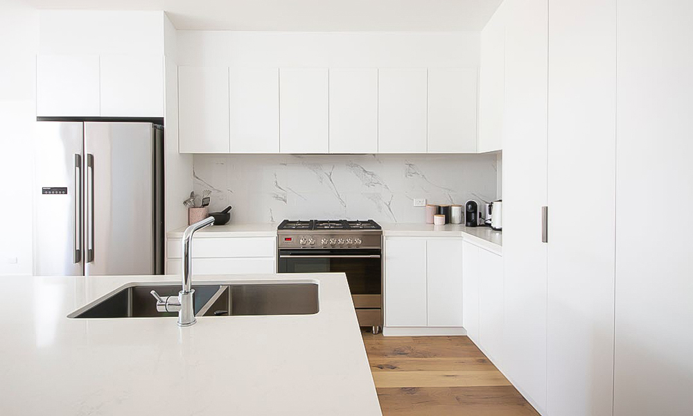 A modern L-shaped kitchen with glossy white lacquered cabinetry and a central island. The sleek white finish creates a bright and airy feel, while the central island enhances both the functionality and design of the space, providing extra workspace and a stylish focal point.