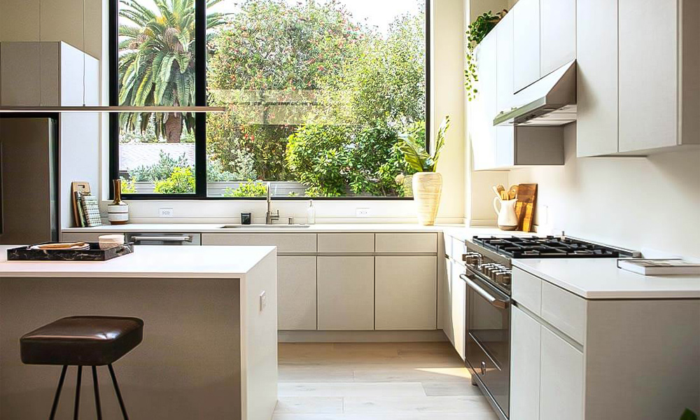 A modern L-shaped kitchen featuring glossy white lacquered cabinetry and a central island. The high-gloss finish of the white cabinets creates a sleek and clean look, while the island adds both style and extra workspace, enhancing the kitchen's functionality.