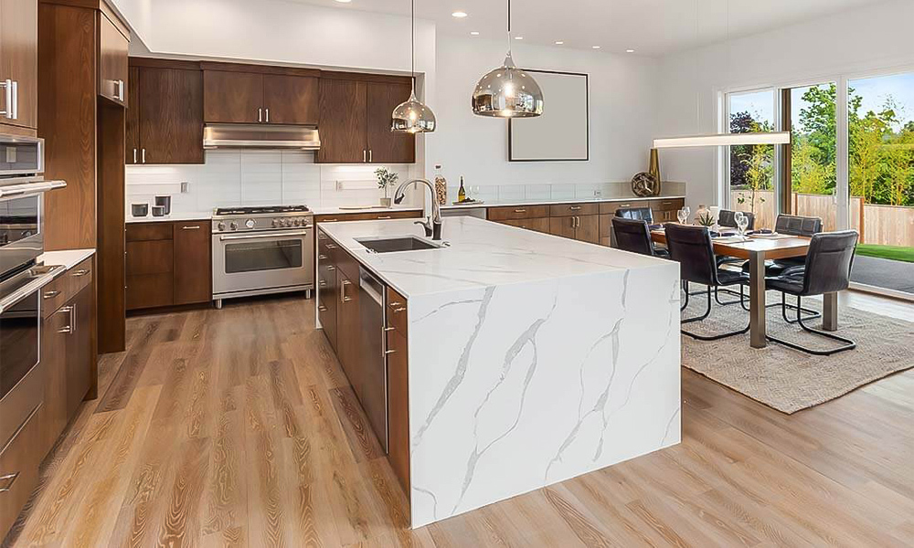 A stylish kitchen featuring wood veneer cabinetry and a central island with a white countertop. The natural warmth of the wood contrasts beautifully with the clean, bright white surface of the island, creating a balanced and inviting modern design.