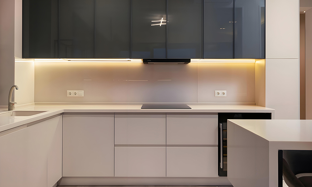 A close-up view of an L-shaped kitchen with glossy white cabinetry and a central island. The bright, reflective surfaces create a sleek and modern atmosphere, while the layout and island provide both style and practical workspace.