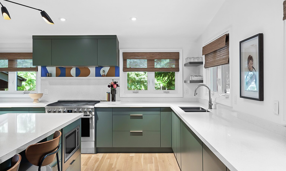 A modern L-shaped kitchen featuring green cabinetry with sleek white countertops and a central island. The fresh green cabinets add a vibrant and refreshing touch, while the white surfaces provide a clean, bright contrast. The central island offers extra workspace and seating, enhancing both functionality and the contemporary style of the kitchen.