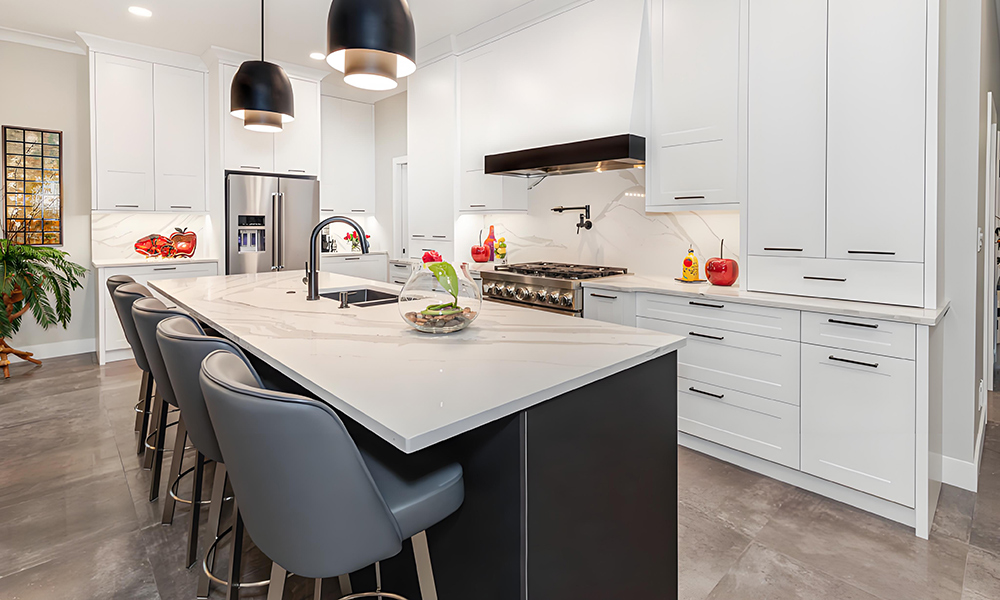 A modern kitchen featuring white lacquered cabinets in an L-shaped layout, complemented by a central island. The glossy white finish of the cabinets enhances the sleek and contemporary feel of the space, while the central island provides additional workspace and storage. The clean lines and minimalist design contribute to an open, airy atmosphere, making this kitchen ideal for both cooking and entertaining. The bright, reflective surfaces create a bright and inviting environment, perfect for a modern home.