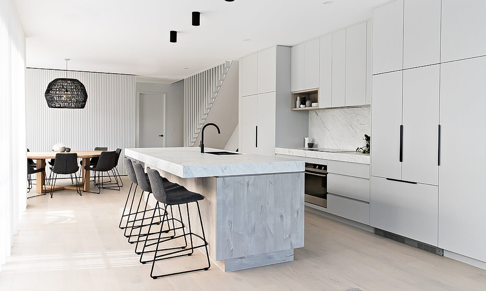 A side view of a one-wall kitchen featuring white lacquer cabinets and a central countertop island. The glossy white finish reflects light beautifully, emphasizing the modern and minimalist design. The central island provides functional workspace and complements the streamlined layout of the kitchen.